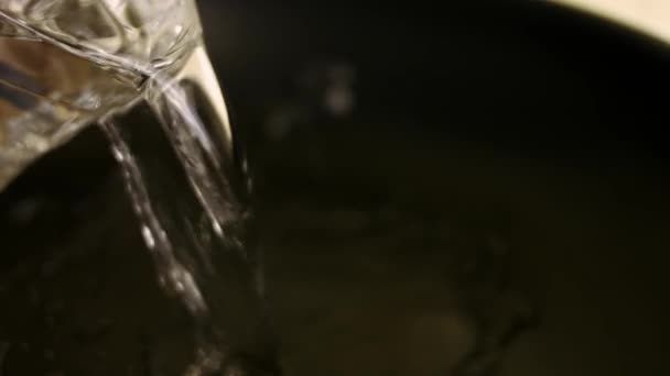 Female chef pouring a glass of water into a frying pan. Preparing the sauce for chicken. Process of cooking shkmeruli - Georgian dish — Stock Video