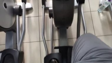 Yürüyen bir simülatör üzerinde alıştırmalar. Bacakların üst görüntüsü. Adam kulübe spor için gidiyor. Akıllı telefondan çekim