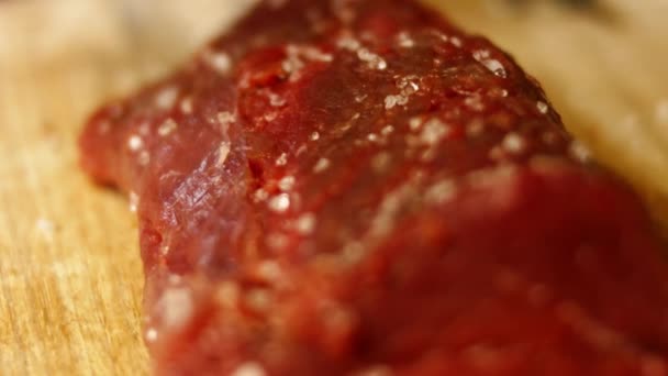 Chef aplicando sal marinho em carne crua. Fogão preparando carne na mesa de cozinha profissional com várias imagens de vegetais 4k — Vídeo de Stock