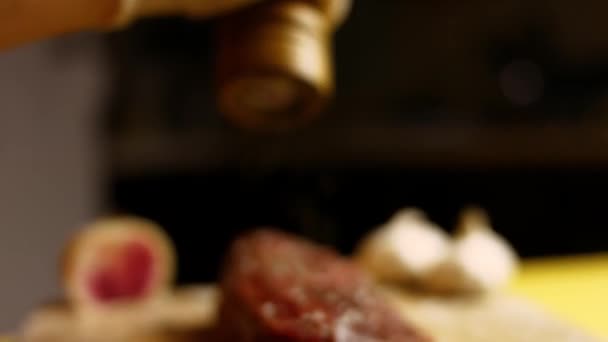 Male tattooed Chef s Hand Seasoning Fresh steak in a Bright Light. Cuisine, Bon Apetite, Fresh Meat, Pepper Salt, Garlic and Rosemary. — Stock Video