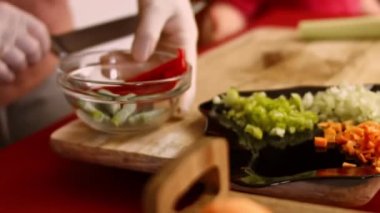 Tahta kesme tahtasının üzerinde donmuş kırmızı dolma biber soyan bir kadının elleri.