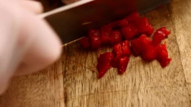 Tahta kesme tahtasının üzerinde donmuş kırmızı dolma biber soyan bir kadının elleri.