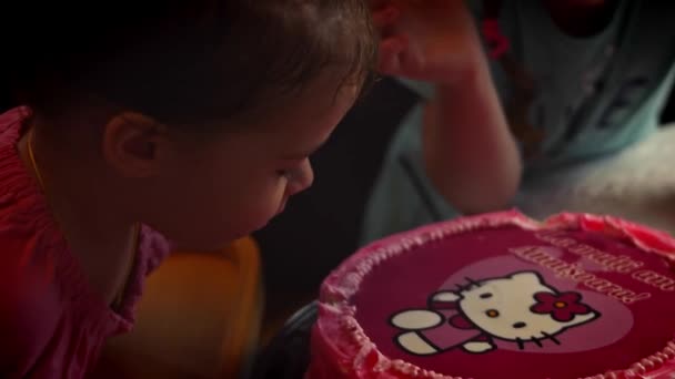 Счастливая маленькая девочка празднует свой день рождения с семьей задувая свечи на своем торте. Родители, бабушка и дедушка смотрят, как маленький ребенок задувает свечи для торта — стоковое видео