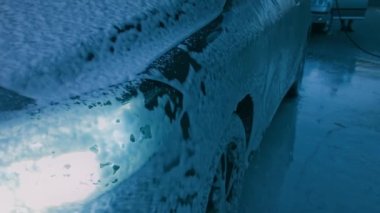 Adam arabayı köpükle yıkar. Gece çekimi