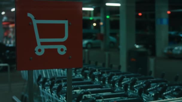 Kov prázdný nákupní košík vlevo na zastřešené podzemní parkoviště nákupního centra. Vozík v supermarketu s rozmazanými zaparkovanými auty na pozadí. 4k noční video silniční značka — Stock video