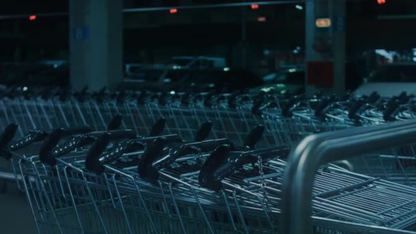 Metal empty shopping cart left at roofed underground parking of shopping mall. Supermarket trolley with blurred parked cars on background. 4k night video road sign — Stock Video