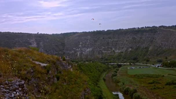 Vedere din spate a unui parașutist care se învârte în aer cu o parașută a aripilor. Acţiune. Scafandru profesionist care trage pe o panoramă de pietre și cer frumos. 4k video — Videoclip de stoc