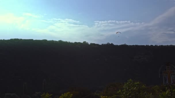 Rear view of a parachutist circling in the air with a wing parachute. Action. Professional sky diver pulling the sling to control the parachute while flying on grey cloudy sky background — Stock Video