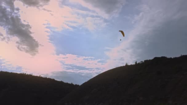 Rear view of a parachutist circling in the air with a wing parachute. Action. Professional sky diver pulling the sling to control the parachute while flying on grey cloudy sky background — Stock Video