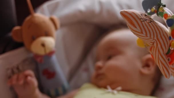 Schöne Nahaufnahme eines niedlichen Neugeborenen, das auf dem Rücken in einem Kinderbett liegt. Verspieltes Porträt eines aufgeregten neugeborenen Kleinkindes beim Betrachten rotierender Spielzeuge. Konzept der Kindheit, des neuen Lebens, der Elternschaft — Stockvideo