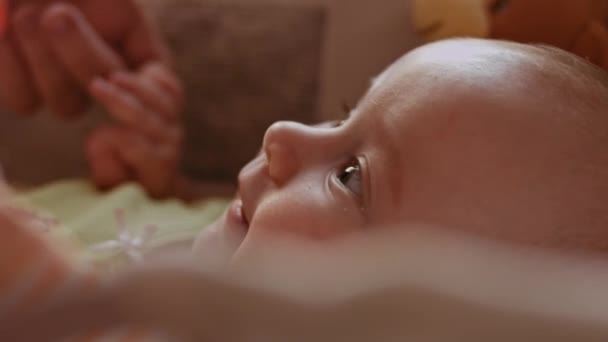 Bellissimo primo piano filmato di un bambino carino appena nato sdraiato sul retro in culla. Ritratto giocoso di un bambino neonato eccitato che guarda giocattoli rotanti. Concetto di Infanzia, Nuova Vita, Genitorialità — Video Stock