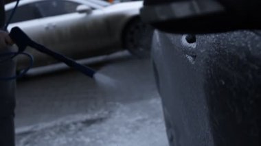 Arabanın dış tarafına köpük saçmak için silahı kullanıyor..
