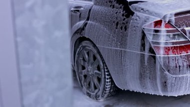 Vitiligo 'su olan genç bir adam oto yıkamada arabanın köpüğünü ve tozunu temizlemek için yüksek basınçlı jet suyu kullanıyor..