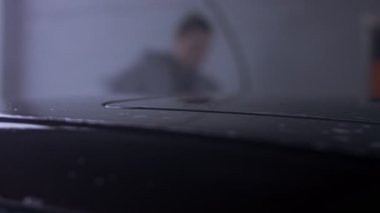 Adam arabanın yüzeyindeki köpüğü temizlemek için yüksek basınçlı jet suyu kullanıyor..