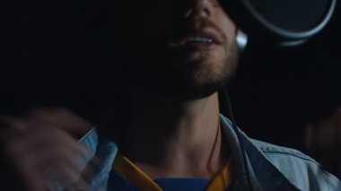 Kulaklıklı erkek rap şarkıcısı modern bir stüdyoda yeni bir şarkı kaydediyor..