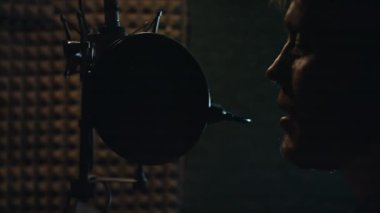 Kayıt stüdyosunda şarkı söyleyen kulaklıklı bir erkek rap şarkıcısının arka plan görüntüsü..