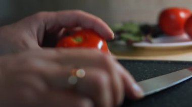 Kadın eli mutfak bıçağı kullanarak taze bir domatesi ikiye böler..