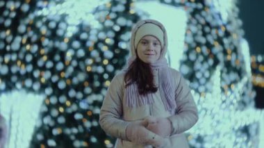 Tatlı kız, kış festivalinde Noel ağacının arka planındaki kameraya bakıyor..
