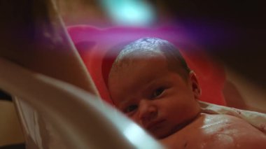 Anne yeni bebeğini nazikçe yıkıyor, bebek sakin.