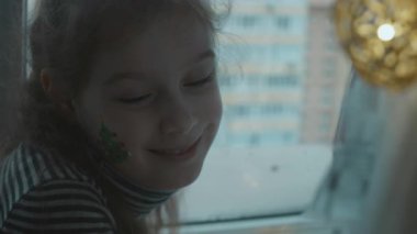 Yüzünde Noel ağacı resmi olan tatlı küçük kız kameraya bakıyor..