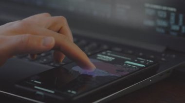 Siber saldırıların görsel göstergeleriyle kaplı dünya haritasını gösteren cep telefonu ekranına dokunan kişi.