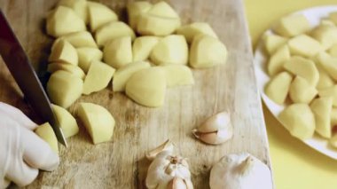 Tahta kesme tahtasının üzerinde patatesler daha küçük parçalara bölünüyor..