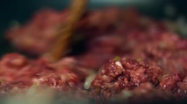 Köfte eti tavada doğranmış soğanla pişiriliyor ve ahşap bir spatulayla karıştırılıyor..