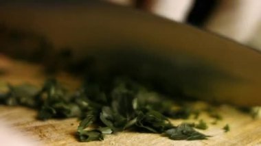 Kişi, tahta kesme tahtasındaki maydanozu ince ince kesmek için keskin bir bıçak kullanıyor..