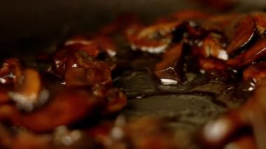 Kızartma tavasında ahşap bir spatulayla karıştırılan sotelenmiş mantarların makro görüntüsü.