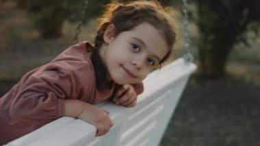 Anaokulu öğrencisi bahçede salıncakta sallanıyor..