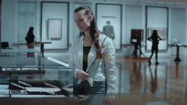 Müzedeki sergiye bakan düşünceli beyaz bir kadın. Arka planda, Sovyetler Birliği zamanının eski nesneleri ve cam altındaki resimler var. 2023, Tarih Müzesi, Chisinau, Moldova.