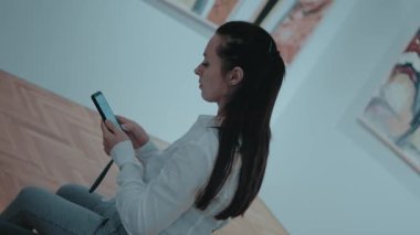 Sanat galerisinde akıllı telefon kullanan genç bir kadın..
