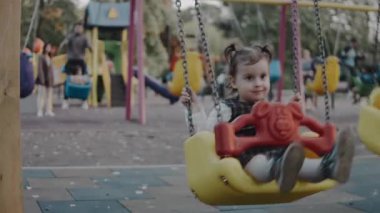 Dışarıda çocuk parkında sallanan sevimli, tapılası bir kız. Mutlu gülümseyen bebek zincirli salıncakta oturuyor.