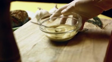 Kişi, tahta kesme tahtasına Dijon hardalı dolu bir cam kase koyar..