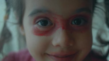 Neşeli kendine güvenen küçük kız yüzünü rujla boyadı ve eğlence için maske yaptı..