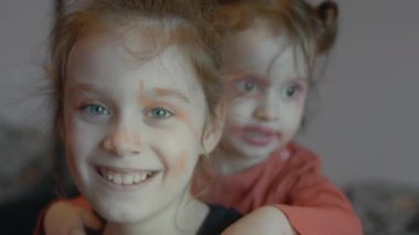 Komik küçük kızlar gülmek ve kameraya bakmak için yüzlerini ruj ve göz farı ile boyadılar..