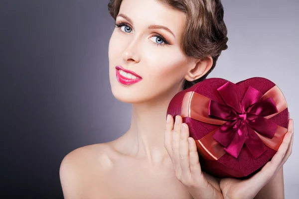 Makyaj ve saç modeli ile kalp şeklinde hediye kutusu ile mutlu güzel model kız. Sevgililer günü