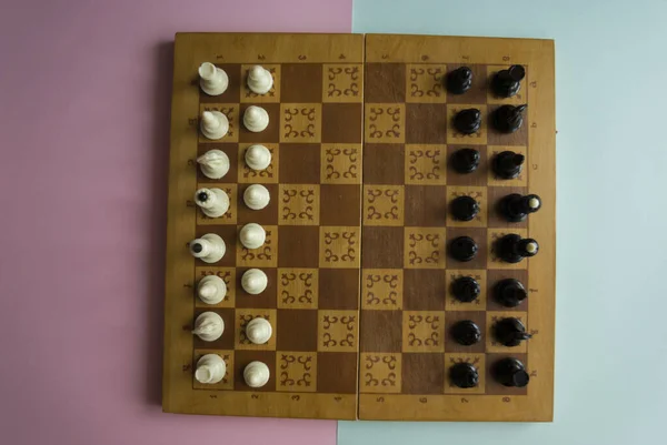 Chess is placed on the chessboard before the start of the game top view on a blue and pink background