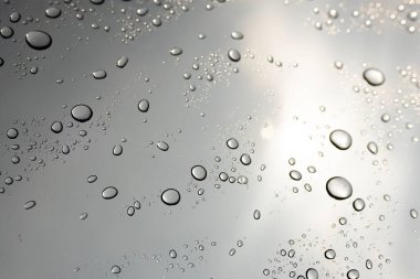 Bulutlu arka planda cam yüzeyine yağmur damlaları düşer. Doğal yağmur damlası deseni. Cam yüzeydeki su damlacıkları
