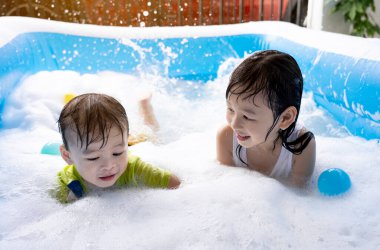 Kız ve erkek kardeş evdeki yüzme havuzunda baloncuklarla oynarken eğleniyorlar. Yaz su oyunu, aile mutluluğu, çocukların mutluluğu.