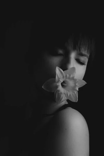 Ağzında çiçek olan ve gözleri kapalı bir kadının siyah beyaz portresi.