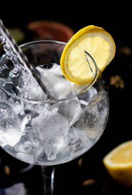 Gintonik hazırlık modunda. Tonik nazikçe bardaktaki buzun üzerine düşer. Süslemek için limon dilimi ile birlikte.