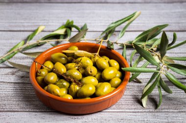 Kahverengi bir seramik kasede zeytinler zarif gri bir kır masasında dekoratif bitkilerle