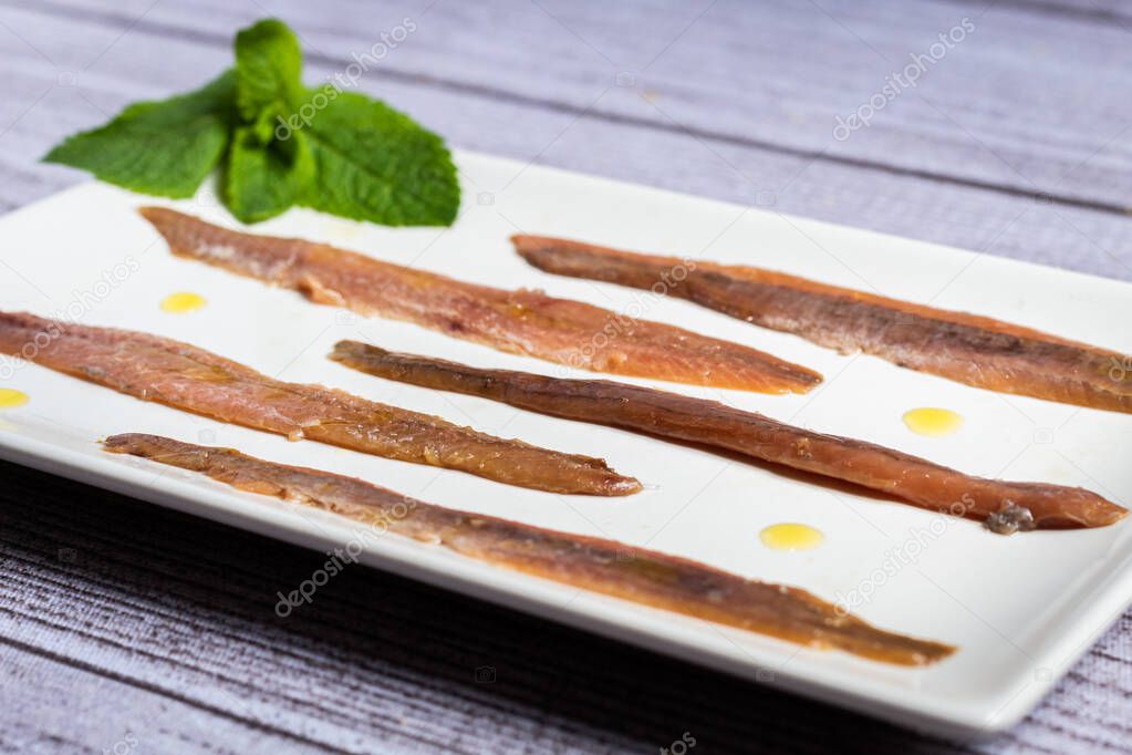 Gourmet anchovies on a white plate and on an elegant gray rustic table