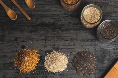 Chia, keten ve kinoa tohumlu üç cam bardak ve onların önünde, dağlar ya da tohum yığınları koyu kırsal masada.