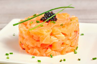 Beyaz bir tabakta soğan ve havyar süslemeli ve açık gri arkaplanlı gurme somon tartar.