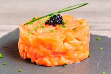 Siyah tahtada soğanlı somon tartar ve havyar ve zarif gri bir kırsal arka plan.