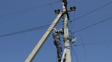 Elektrik işi, elektrik direğini tamir eden adam tüm güvenlik ekipmanlarını giyiyor.