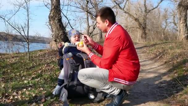 Apa kanállal eteti a gyereket, miközben a szabadban sétál. — Stock videók