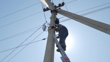 Elektrikli siluet mühendisi merdivenlerde duran elektrik direği üzerinde çalışıyor.
